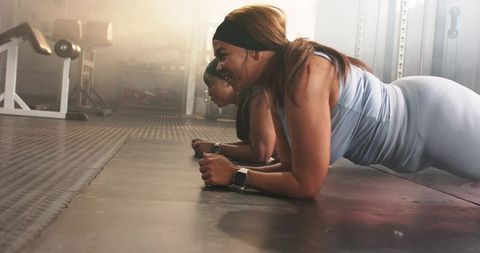 Two fit women holding forearm plank together in gym, strengthening core and team motivation