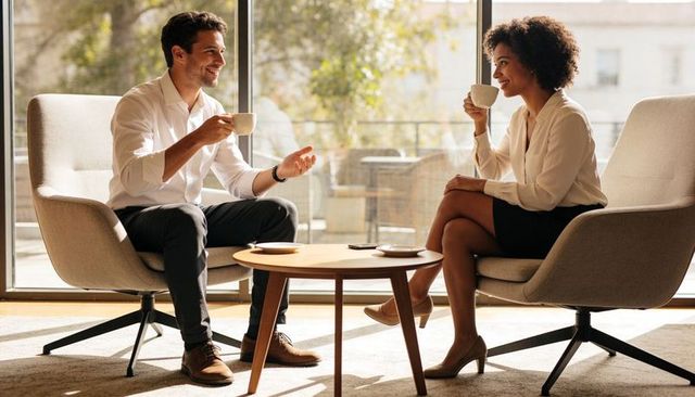 Two professionals chatting over coffee in modern office lounge, relaxed business meeting