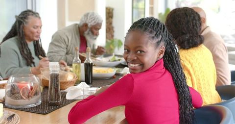 Smiling girl sharing meal with multigenerational family gathering at wooden dining table
