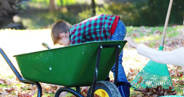 Child playing outside in garden with a wheelbarrow and rake. Great for depicting outdoor activities, autumn season, children’s play, and family bonding moments. Suitable for use in kid-friendly, educational, or lifestyle content.