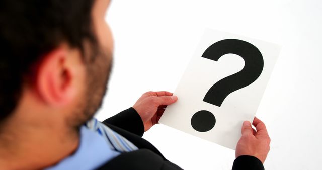 A Caucasian man is holding a paper with a large question mark printed on it, with copy space. His pose suggests he is seeking answers or presenting a query, emphasizing concepts of curiosity, uncertainty, or decision-making.
