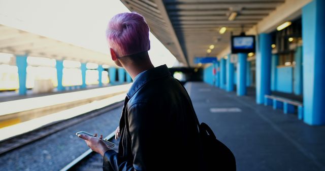 Young Caucasian woman waits at a train station, with copy space. Her vibrant hair adds a pop of color to the travel scene.