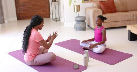 Mother and daughter practicing yoga at home on mats — family fitness and mindfulness