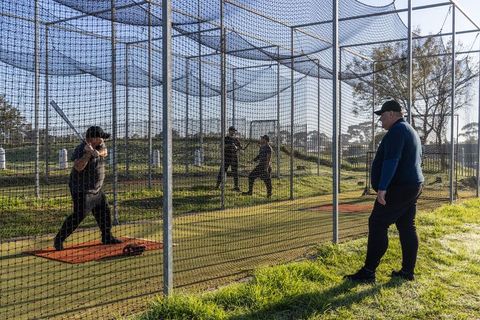 Batter practicing in outdoor batting cage while coach calling pitches at baseball training