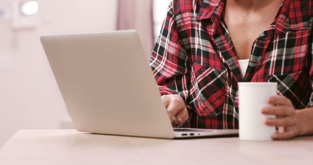 Person working on laptop while holding coffee cup at home desk - Download Free Stock Images Pikwizard.com