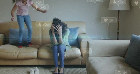 Stressed mother covering face while child jumping on sofa with social media overlay