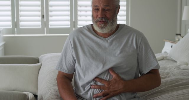 Senior African American man with stomach pain sitting on bed - Download Free Stock Images Pikwizard.com