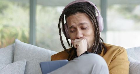 African american man listening with headphones and reacting emotionally while using tablet at home