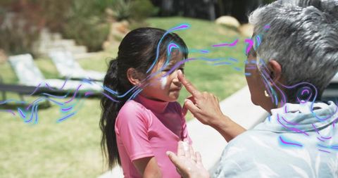 Senior Man Applying Sunscreen to Young Girl in Backyard, Sun Safety and Family Bonding