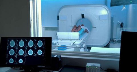 Adult undergoing mri scan in modern radiology control room showing brain scans on monitor