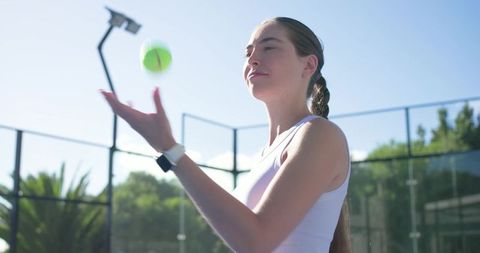 Woman tennis player tossing ball preparing serve on sunny outdoor court wearing smartwatch