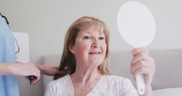 Senior woman receiving grooming assistance at home from caregiver. Scene ideal for articles or promotional material about elderly care, daily routines of senior citizens, home assistance, and health care for seniors. Emotion-focused content showing care and personal support.