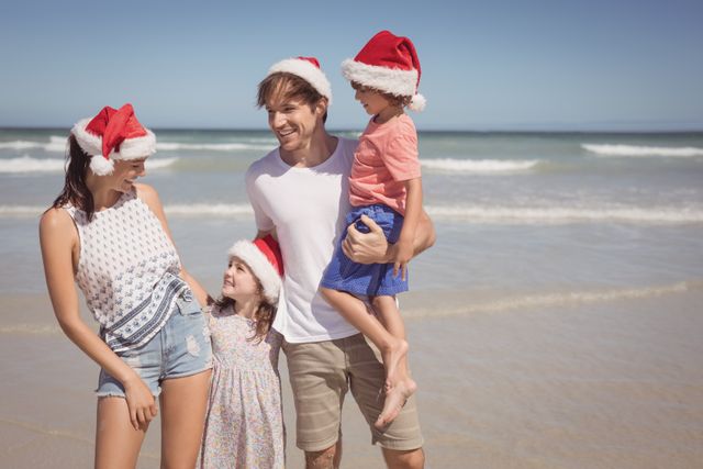Family of four enjoying a sunny day at the beach wearing Santa hats, creating a unique and memorable Christmas experience. Suitable for holiday cards, travel advertisements, family-related content, or promotions highlighting festive vacation spots.