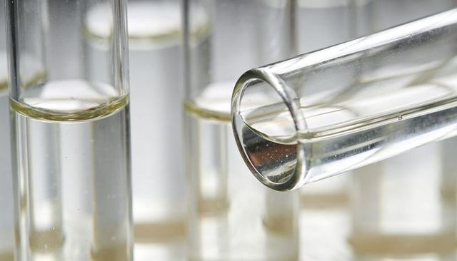 Close-up clear test tube pouring transparent liquid into lab rack with backlit reflections