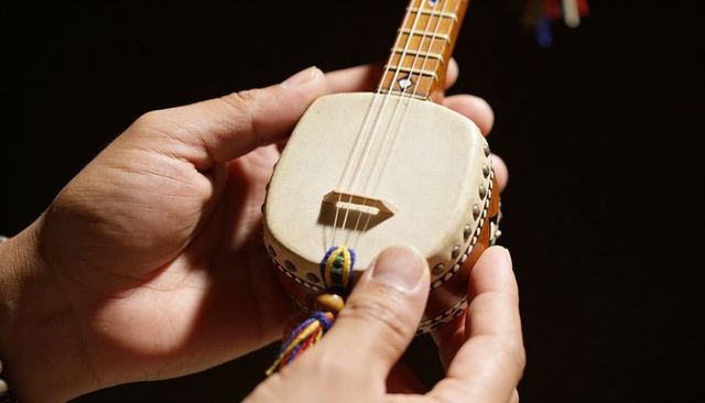 Cradling miniature lute with decorative tassel and beaded bracelet, warm intimate close-up