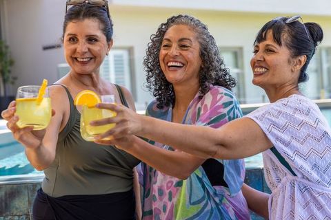 Multicultural women clinking citrus cocktails, raising glasses poolside on summer getaway