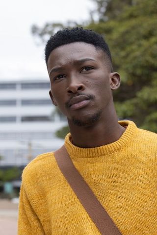 Thoughtful young man wearing mustard sweater gazing on urban campus courtyard
