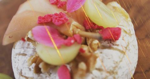 Artisan brie wheel topping with walnuts, grape halves and rose petals on wooden board