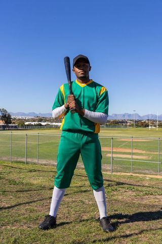 African american baseball player standing and holding bat on sunlit field team portrait