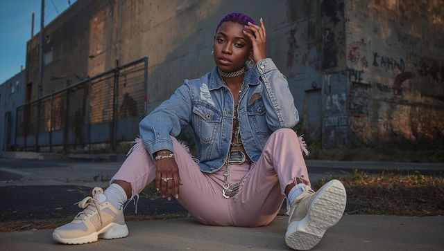 Urban street style portrait of young woman wearing denim jacket and chain jewelry at dusk