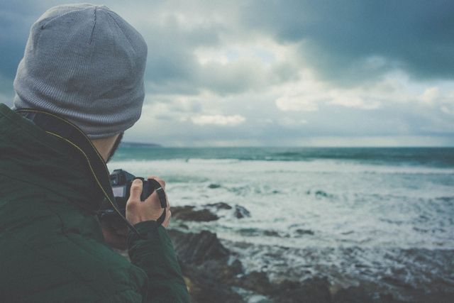 Man in Green Hoodie Holding Dslr Camera Near Seashore Under Gray Clouds - Download Free Stock Photos Pikwizard.com