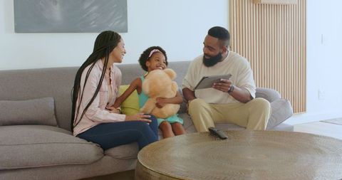 Family bonding on sofa with tablet and teddy bear play