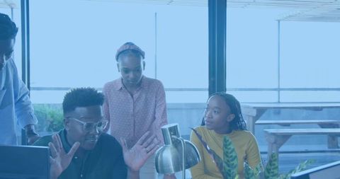 Diverse team collaborating around desk with computer and plants in bright modern office