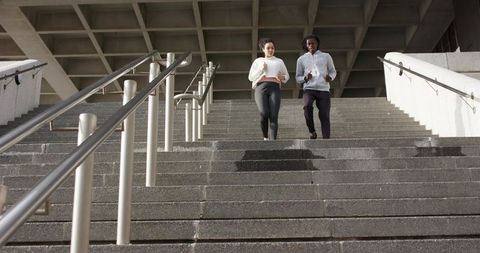 Diverse duo jogging down wide concrete staircase for urban fitness and stair training