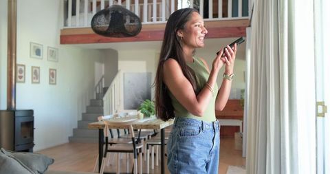 African american woman smiling and using smartphone by sliding door in modern rustic home