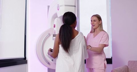 Technologist guiding patient during mammogram exam in pink clinic radiology room
