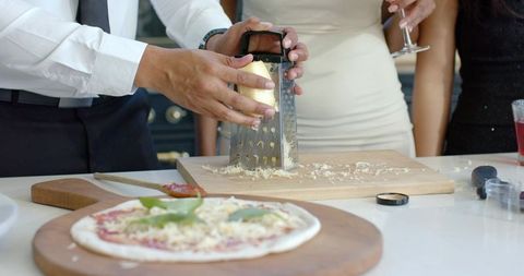 African american couple grating cheese preparing homemade pizza during kitchen gathering