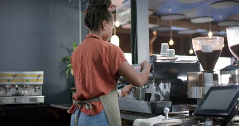 African barista steaming milk and preparing espresso at rustic coffee counter