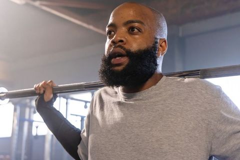 African american man performing heavy back squat with spotter in gym strength training