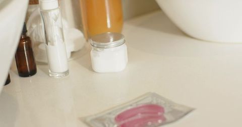 Minimal skincare flatlay with white cream jar and pink gel eye patches on glossy vanity