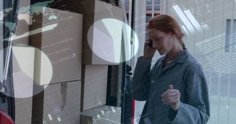 A female logistics worker, wearing uniform clothing, uses the phone while inspecting packages in a van. The digital overlay of graphs and analytics signifies advanced technology integration in logistics as she ensures safe and efficient delivery. Useful for illustrating the role of technology and efficient communication in the modern logistics and transportation sector.