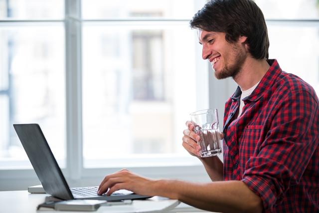 Male business executive having a glass of water while using laptop in office