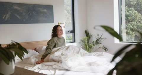 Woman Relaxing on Bed with Indoor Plants in Bright Bedroom