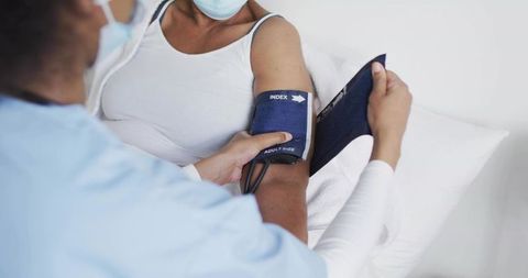 Nurse measuring blood pressure on senior patient in exam bed with blue cuff