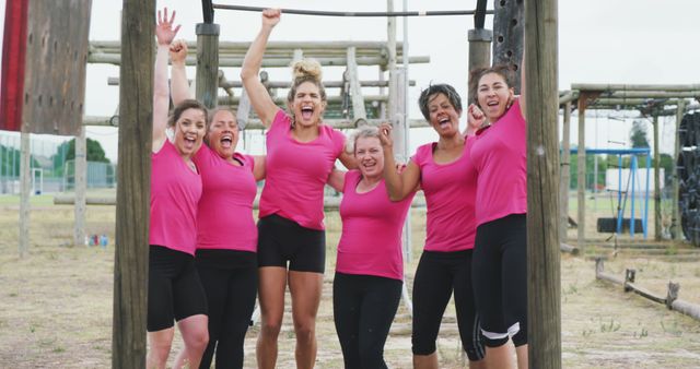 Group of enthusiastic women in matching pink shirts rejoicing after completing an obstacle course. Perfect for themes around team building, women's fitness, outdoor activities, and celebrating achievements. Ideal for promoting fitness programs, team challenges, or motivational events.