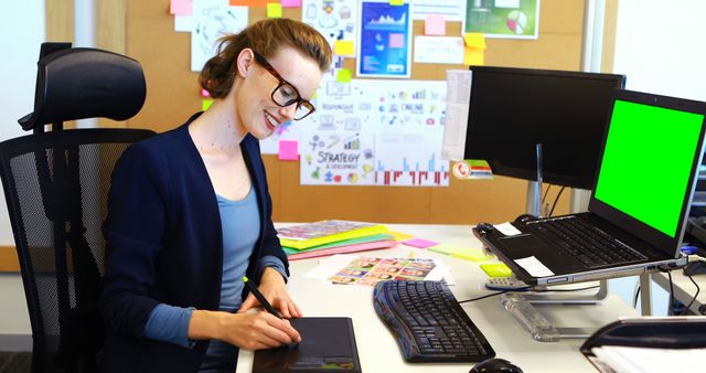 Graphic designer creating digital artwork on a tablet in a modern office. Ideal for use in articles about creative professions, office productivity, or digital illustration tutorials. Perfect for websites showcasing office environments, remote work settings, or creative business solutions.