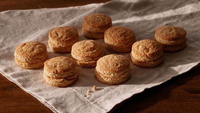 Golden buttermilk biscuits resting on linen cloth rustic kitchen tabletop with crumbs