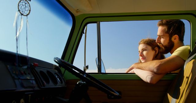 Couple leaning out the window of a vintage green van, admiring the sunset. This image portrays elements of a summer road trip, relaxation, and a sense of adventure. It can be used for travel promotions, lifestyle blogs, or marketing campaigns related to automotive nostalgia and outdoor exploration.