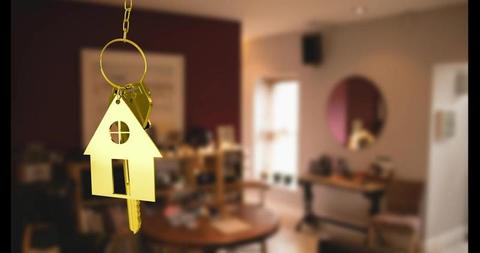 Golden house key and keyring in foreground against blurred view of modern living room, suitable for real estate advertisements, home buying guides, property ownership illustrations, and moving day promotions.