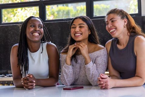 Three friends laughing and leaning on kitchen counter with smartphone