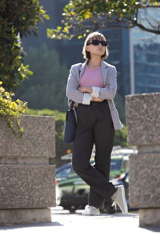 Confident urban professional woman standing in sunlit plaza wearing blazer and sunglasses