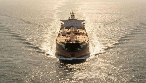 Aerial tanker gliding through golden sea at sunrise, symmetrical bow wave and deck piping