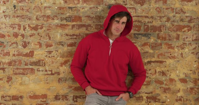 A young man in a red hoodie is leaning against a brick wall, showcasing a casual and confident look. The image emphasizes casual fashion and can be used in promotions for autumn wear, fashion blogs, or lifestyle articles. It highlights trendy outfits and informal styles for young adults.