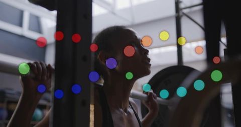 Backlit female lifter bracing for squat with barbell in industrial gym silhouette, intensity