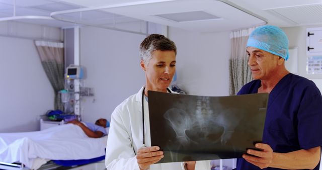 Doctors discussing and analyzing an X-ray in a hospital room with a patient in the background. Useful for topics related to medical care, hospital settings, teamwork in healthcare, and medical diagnostics.