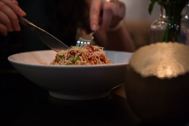 Person enjoying a delicious pasta dish in a cozy restaurant setting. Ideal for use in food blogs, restaurant promotions, culinary websites, and dining-related advertisements.